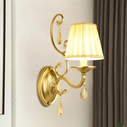 Modern gold fabric wall sconce light fixture with tapered surface, pleated cream lampshade, and crystal accents