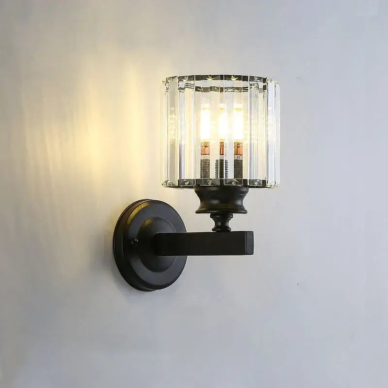 Black metal wall lamp with cylindrical crystal glass shade and three illuminated bulbs for modern living room sconce