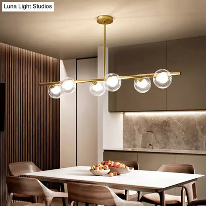 Modern gold finish linear pendant light with five clear glass globes suspended from a sleek horizontal bar