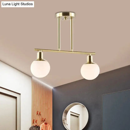 Modern brass-finished linear chandelier pendant light with two spherical milk glass globes and gold finish