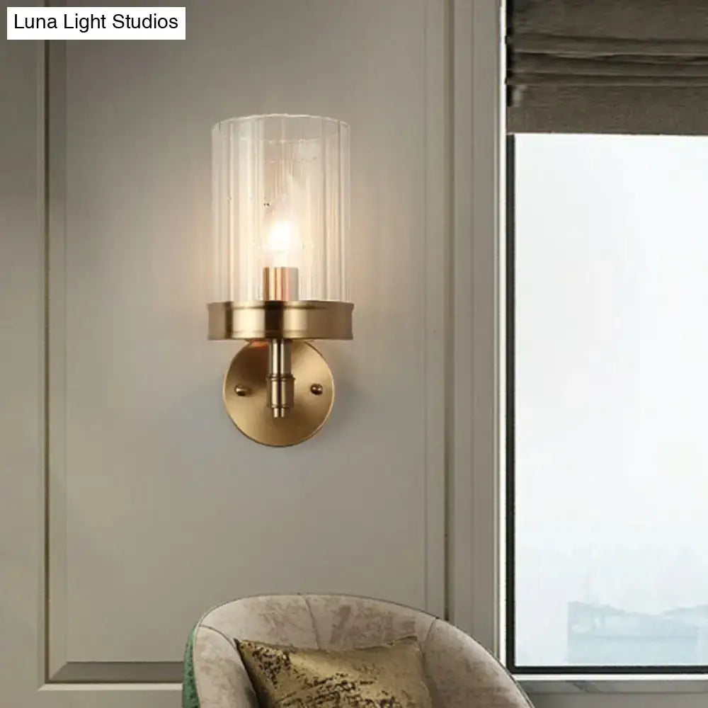 A warm-toned modern gold finish wall light with brass base and clear glass shade showing soft color temperature