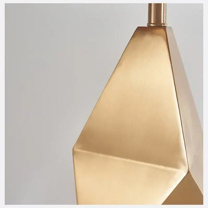 A modern gold geometric table lamp with a sleek three-dimensional faceted brushed finish for bedroom nightstand use