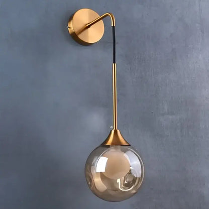 Modern gold wall sconce with a sleek curved arm and amber glass ball shade perfect for decorbites glass ball lighting