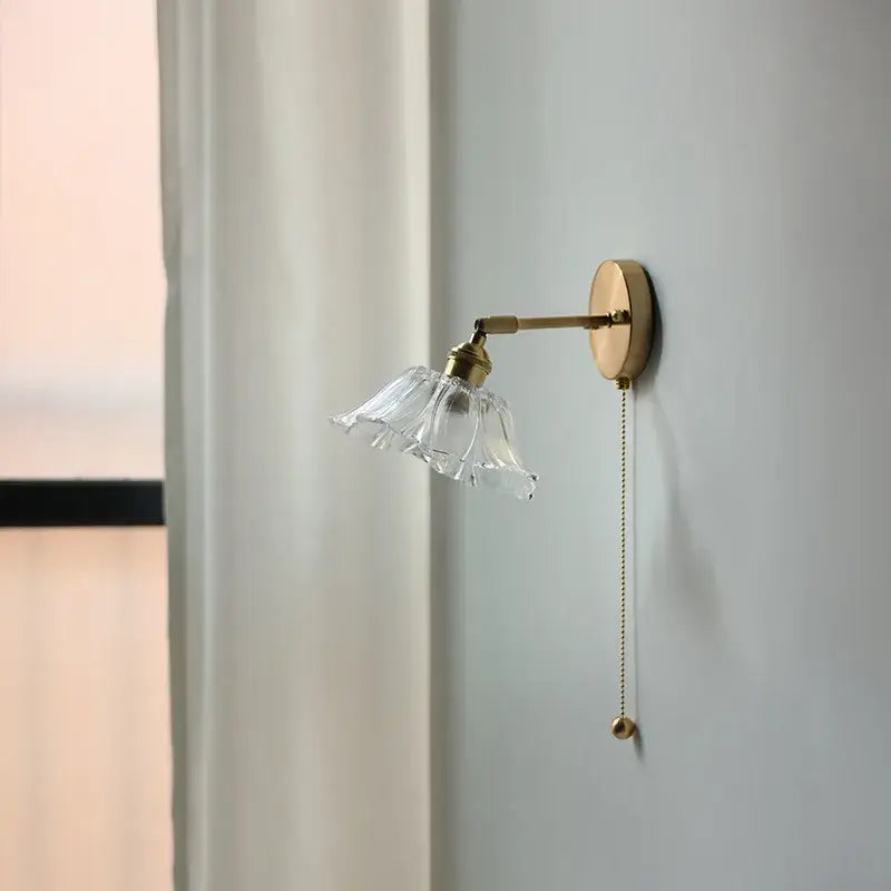 Modern gold wall light with a delicate brass frame, clear fluted glass shade, and an attached bedroom pull chain LED wall light