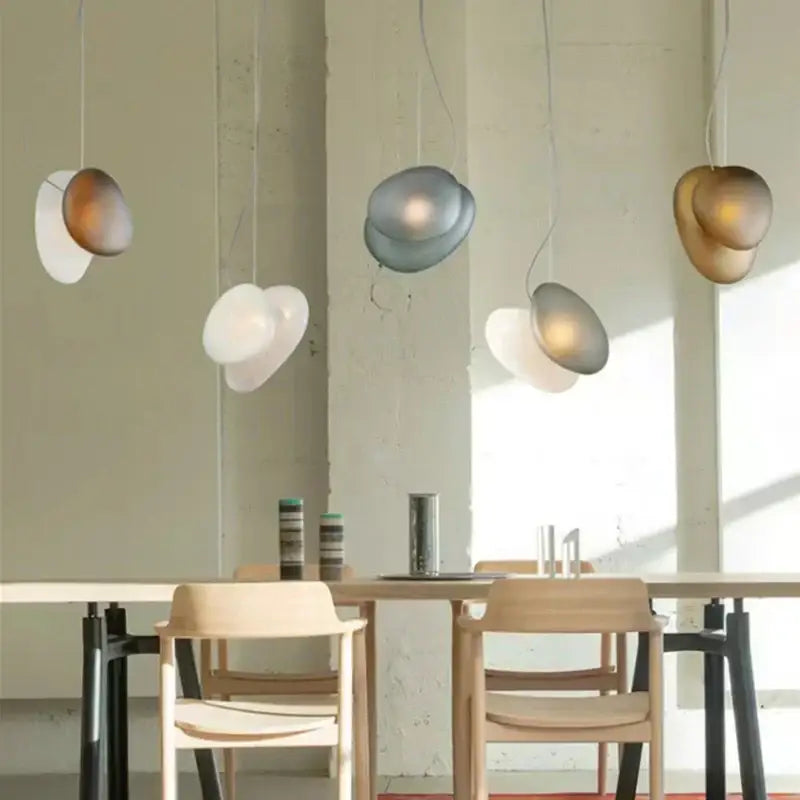 Modern gold and gray glass indoor pendant lights with smooth rounded shades hang above a minimalist dining table