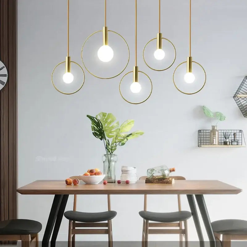 Modern gold-toned decorbites ins wind single pendant light with circular frames hanging above a wooden dining table