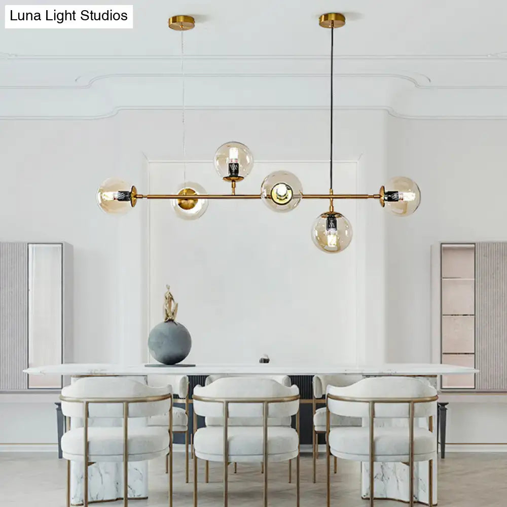 Modern gold island pendant light with six clear glass globes suspended from a central rod for dining room use