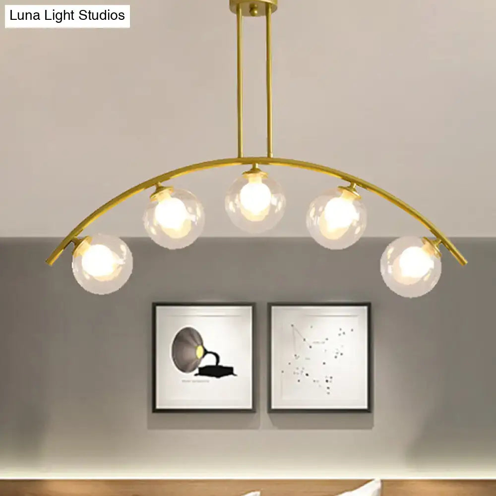 Gold-toned decorbites island pendant with five clear white shade glass globes and curvy modern design for kitchens