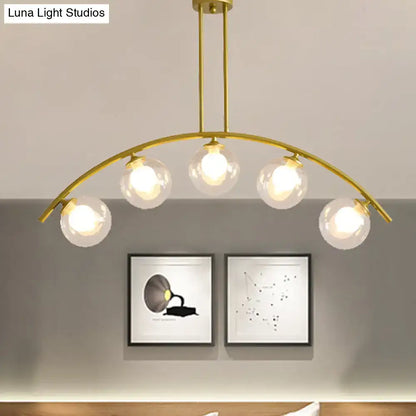 Gold-toned decorbites island pendant with five clear white shade glass globes and curvy modern design for kitchens