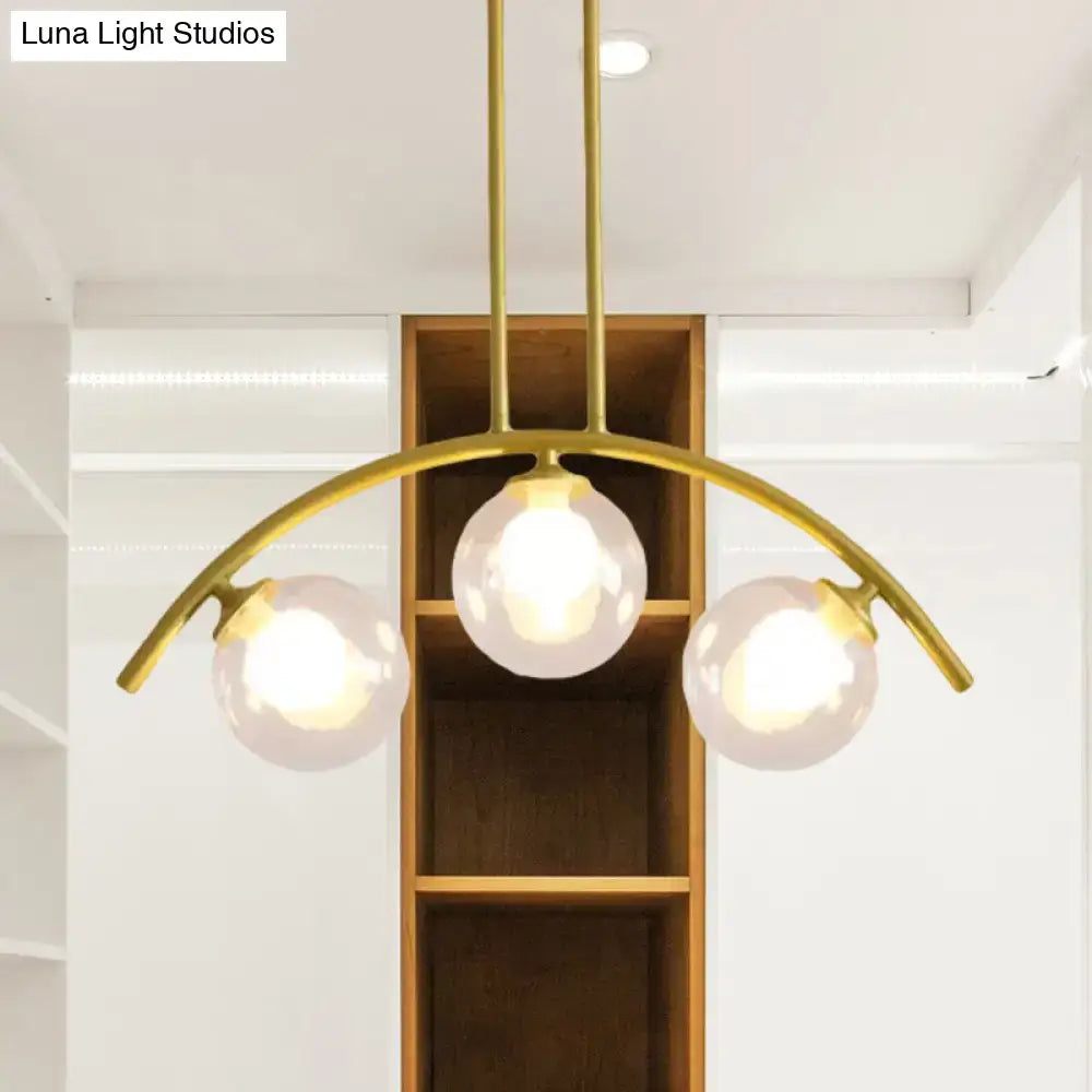 Gold-toned decorbites island pendant with three frosted glass globe bulbs and clear white shade for modern kitchens