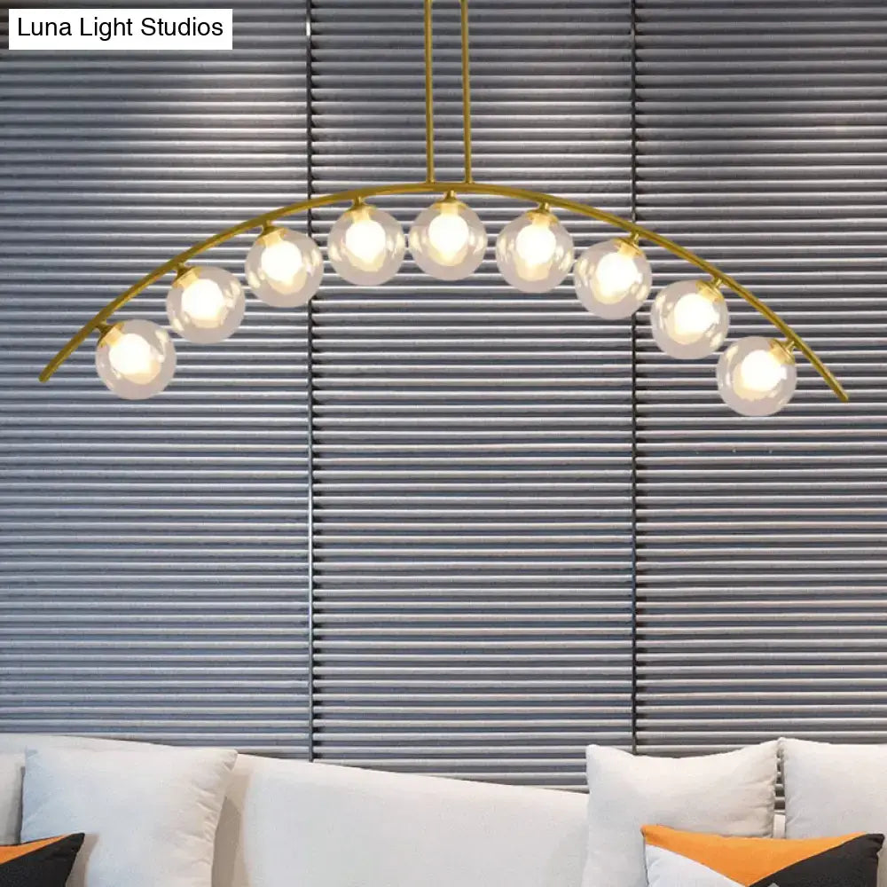 Gold-toned decorbites island pendant with nine glowing spherical glass bulbs and clear white shade for modern kitchens