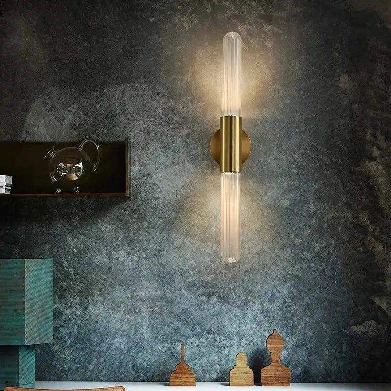 A modern led sconce with a brushed brass base and clear white glass tubes for warm bedroom wall lighting
