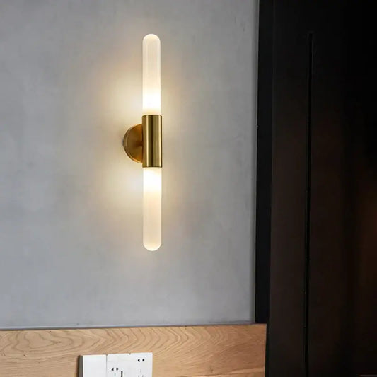 A modern gold led sconce with clear white glass frosted tube and brass-finished metal base for bedroom wall light