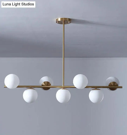 Modern gold metal pendant light with six frosted white glass globe bulbs in a linear design for dining room island