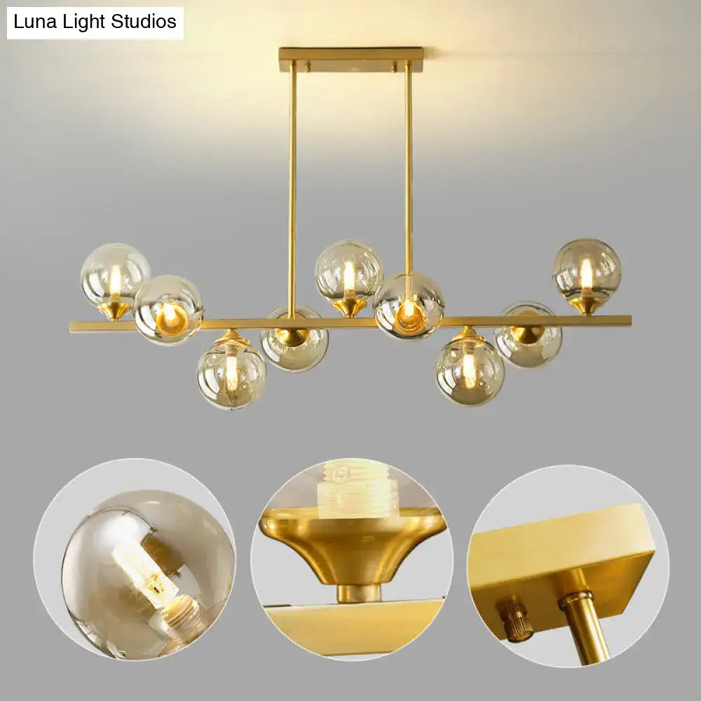 Modern gold metal chandelier with spherical amber glass bulbs suspended from a horizontal bar for dining room island lighting