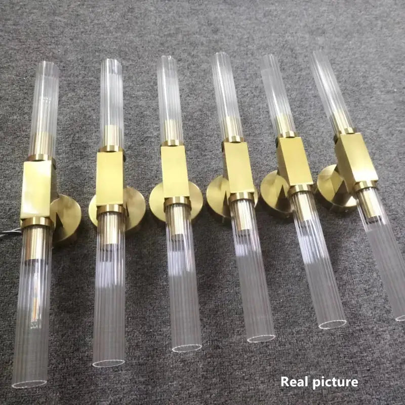Six modern wall sconce lights with clear ribbed glass tubes and polished gold metal fixtures for bathroom use