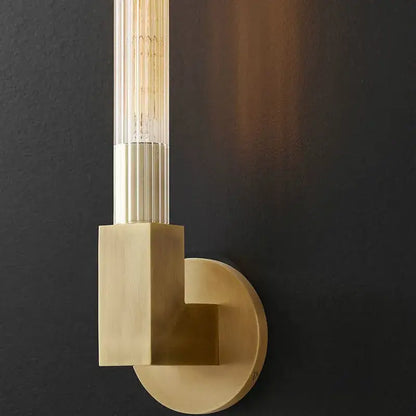 Modern gold metal and glass wall sconce light featuring a brass cylindrical glass shade with an exposed filament bulb
