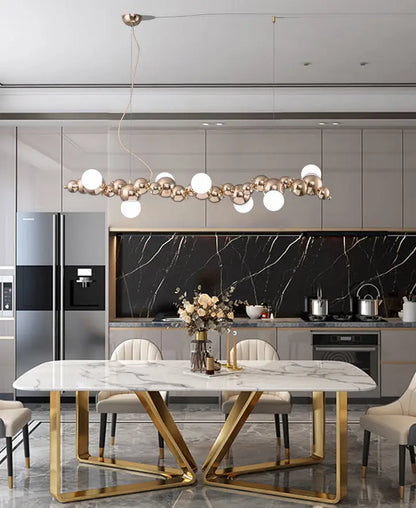 Modern gold metal ceiling light with six elongated spherical pendants hanging above dining room table