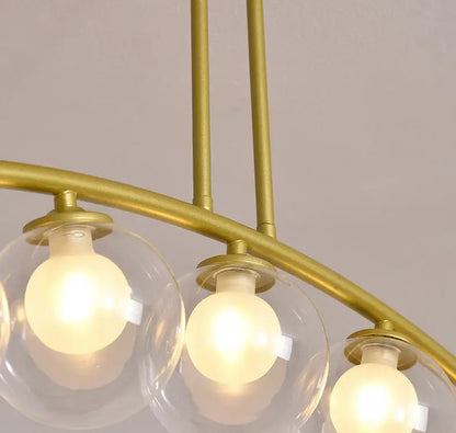 Modern gold metal arched ceiling light with three clear glass globes and warm bulbs for dining room illumination