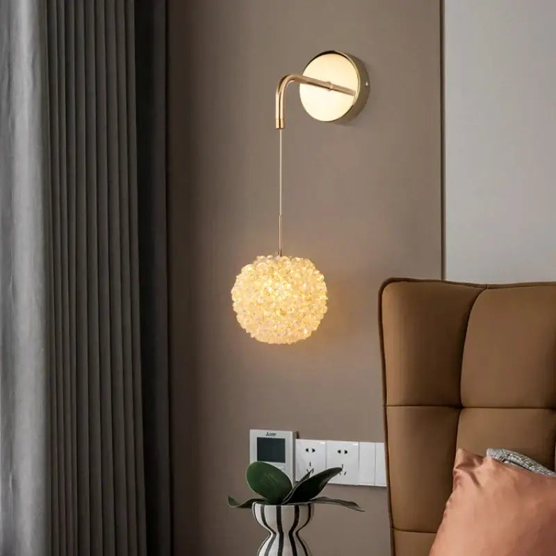 Modern gold metal crystal wall light bedroom sconce with gold-toned curved arm and spherical crystal-encrusted lampshade