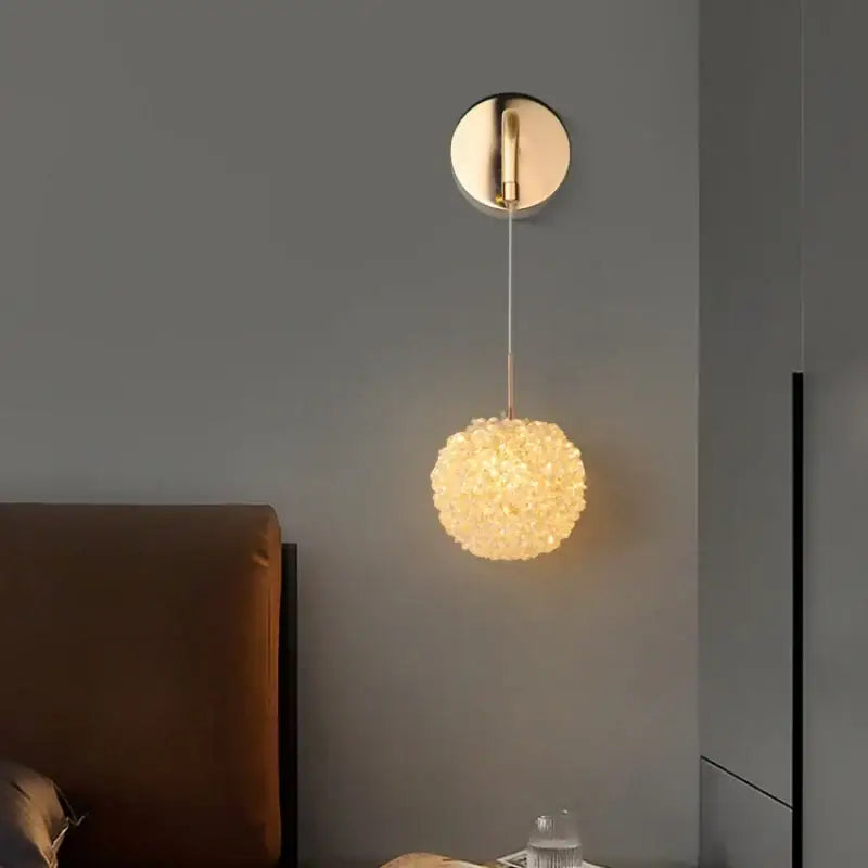A warm glowing spherical pendant wall light with gold metal crystal textured glass for modern bedroom decorbites use