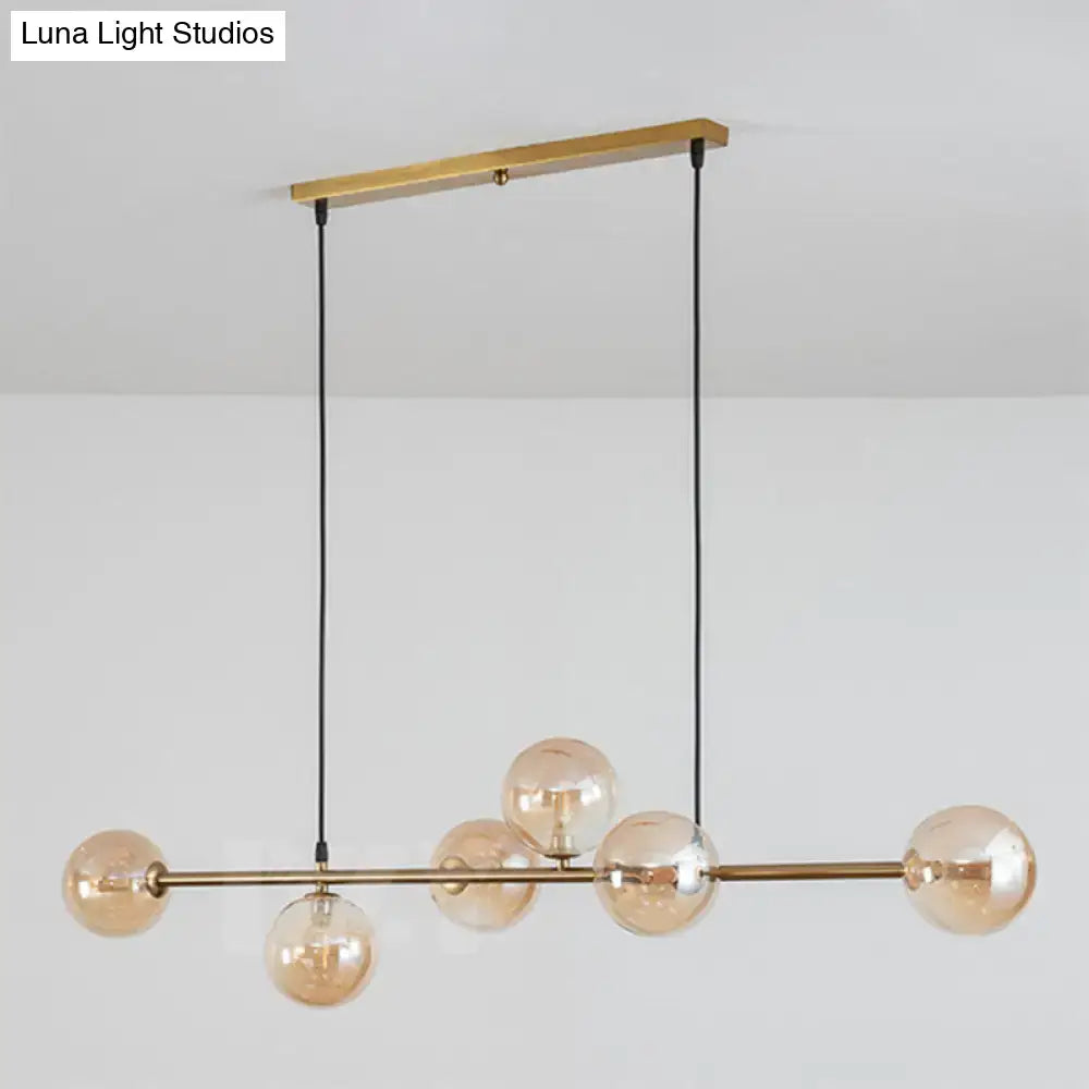 Modern gold metal island pendant with six amber glass globes suspended by black cords for dining room lighting