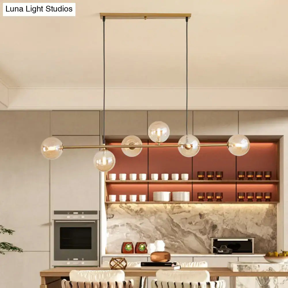 Modern gold metal island pendant featuring a brass bar with five clear glass globe bulbs suspended by black cords