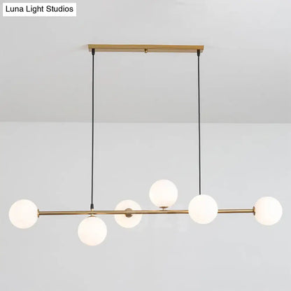 Modern gold metal island pendant with five frosted glass globe bulbs suspended by black cords for dining room