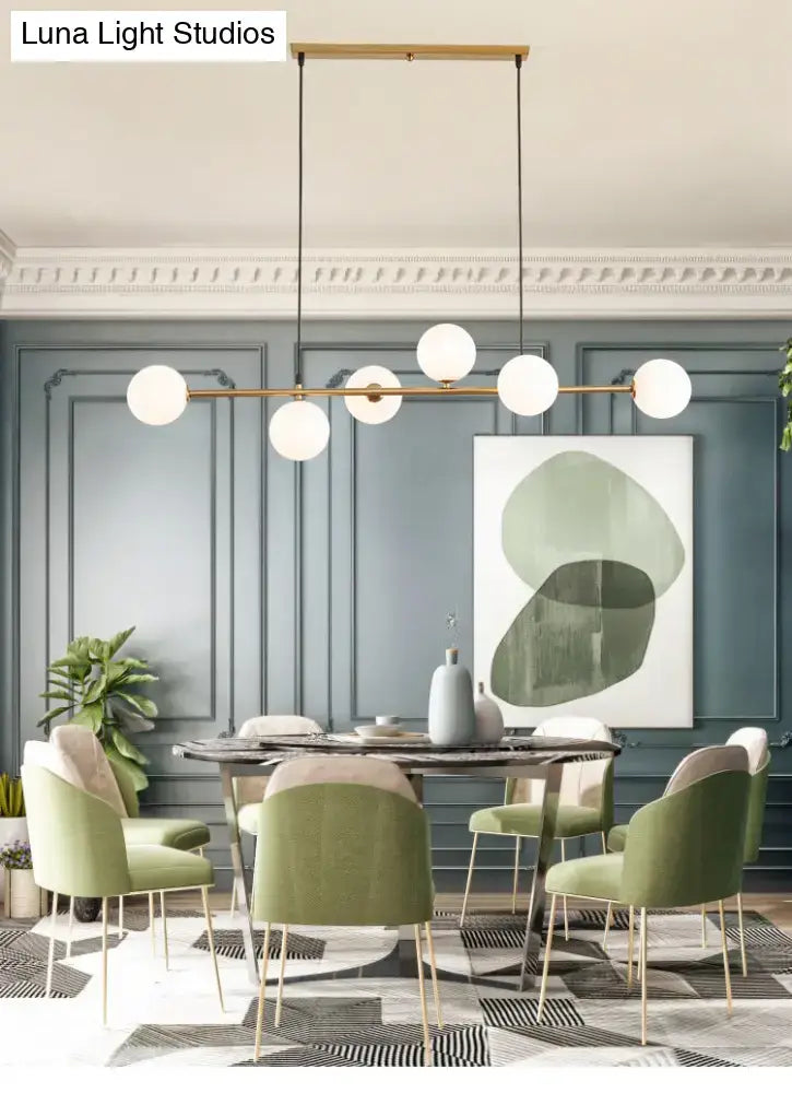 Modern gold metal island pendant featuring a sleek brass frame with six white glass globes for dining room use