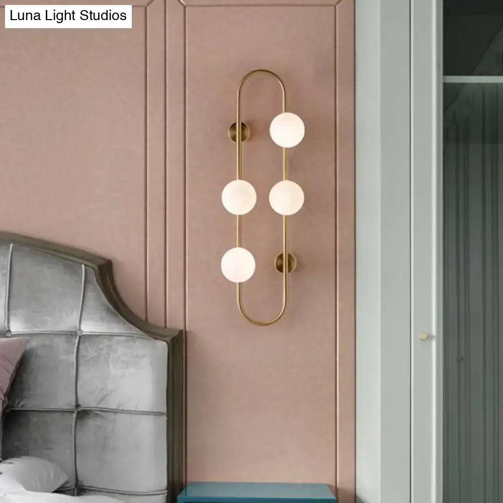 Modern gold wall light with four frosted milky glass shade globes in a curved bedroom sconce design