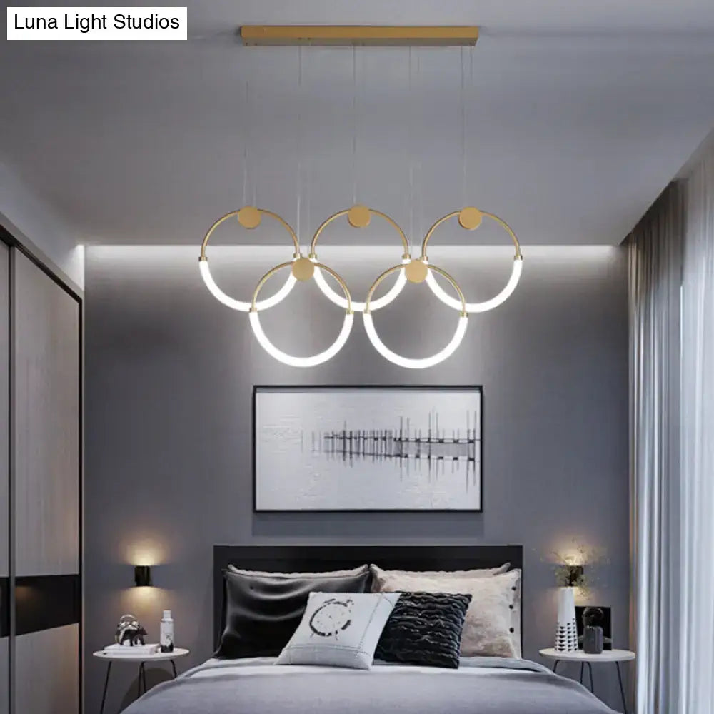 Modern gold minimalistic ring pendant light with illuminated circular rings suspended from wooden ceiling bar