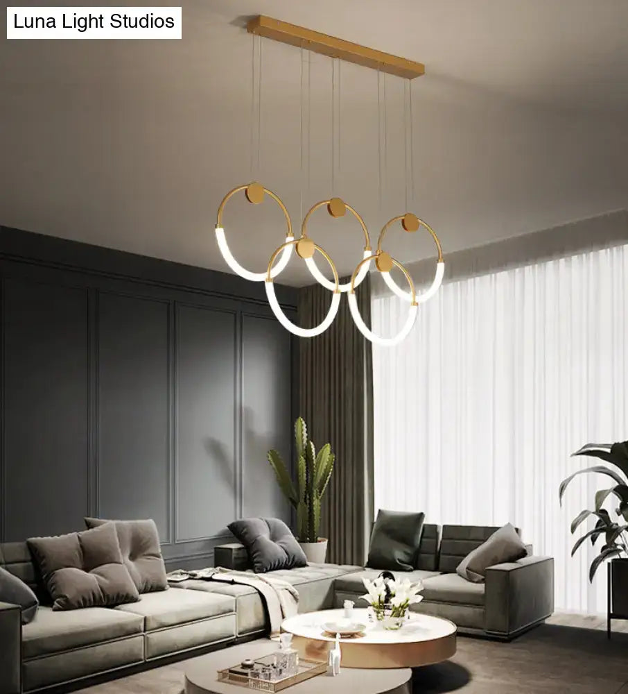 Modern gold minimalistic ring pendant light with three interlocking circular rings and wooden ceiling mount for living room