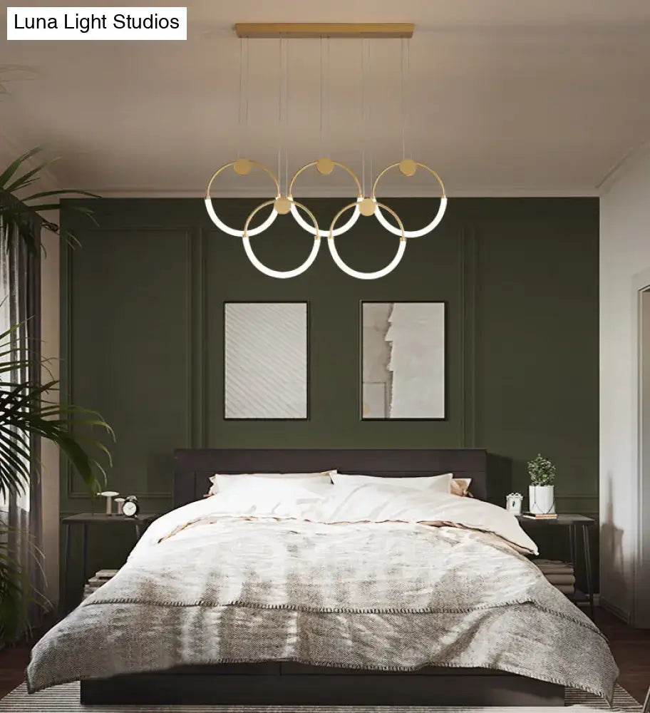 Modern gold minimalistic ring pendant light with illuminated circular rings suspended above a bed for living room