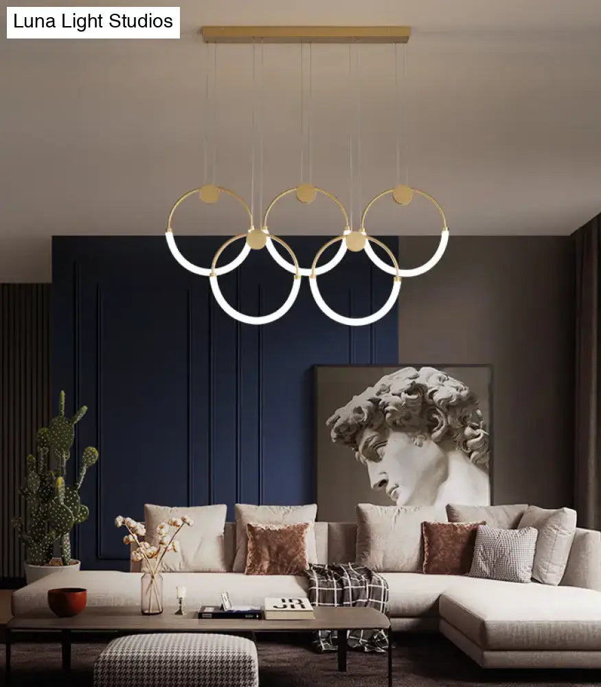 Modern gold minimalistic ring pendant light with illuminated circular rings suspended from wooden ceiling fixture