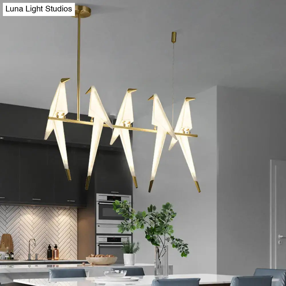 Modern gold origami bird pendant light with illuminated white paper-like wings for dining room decor
