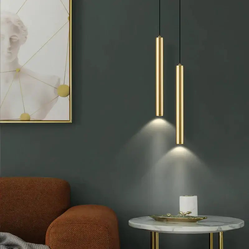 Two sleek cylindrical gold pendant lights hang from the ceiling as part of a modern wall sconce set for bedroom lighting