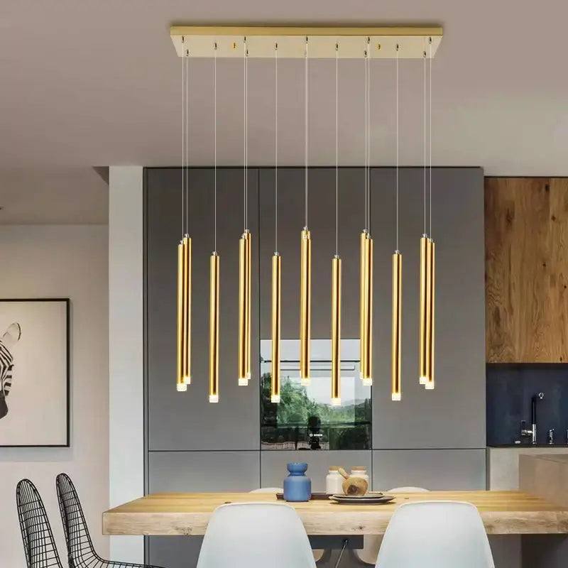 Modern gold-toned cylindrical pendant lights hang from a rectangular fixture in a dining room decorbites elegant chandelier