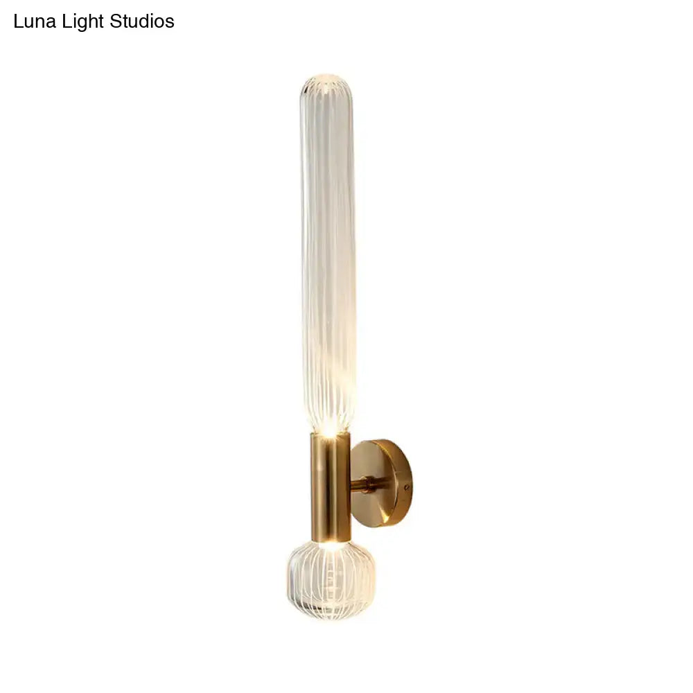 Modern gold ribbed glass wall lighting fixture with a tall cylinder and spherical base illuminated by warm light