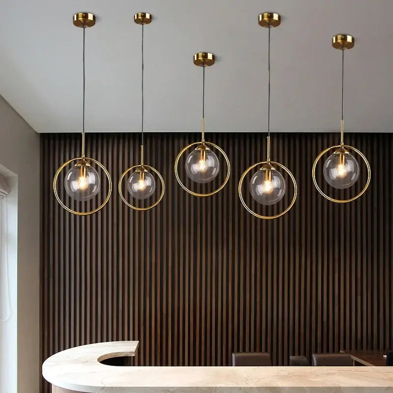 Five modern gold ring glass globe pendant lights with metal frames hang from the ceiling in a dining room setting
