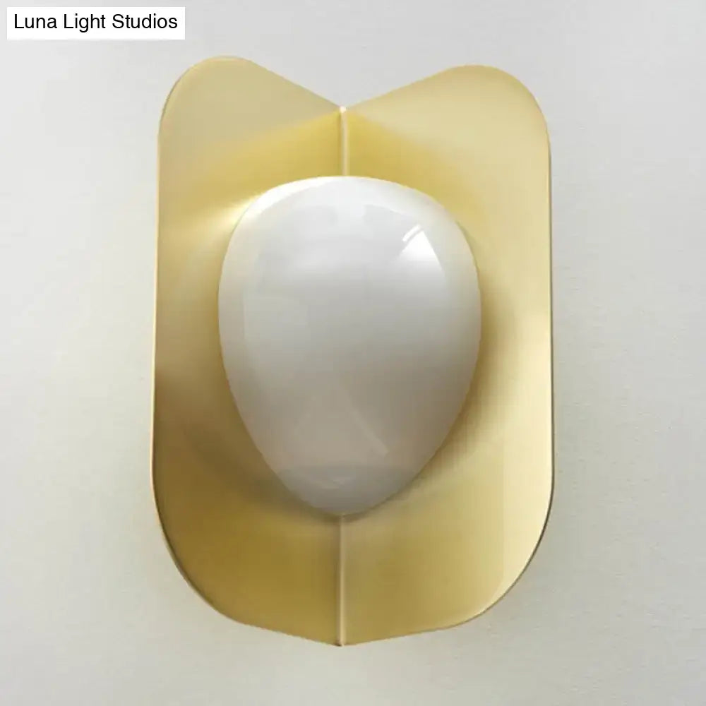 Modern gold sconce light with a gold-toned curved metal shade and smooth white oval glass for bedroom illumination