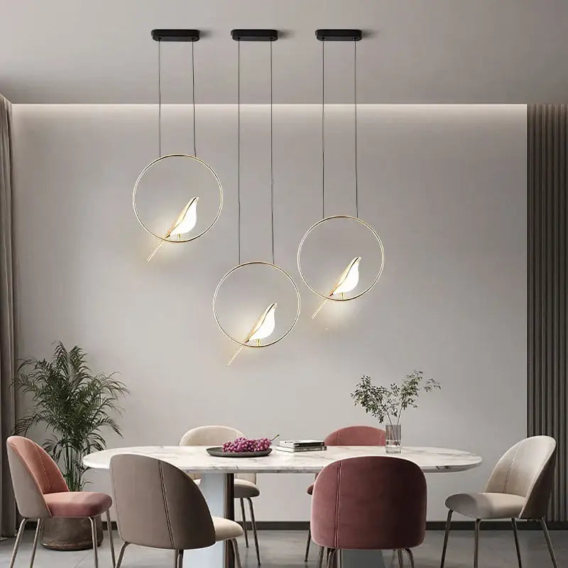 Three modern pendant lights with sleek circular frames and metallic finish featuring minimalist gold and silver magpie silhouettes for lighting area use