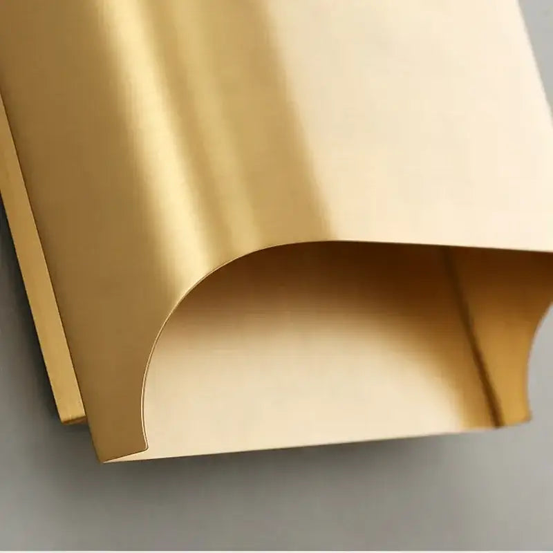 A sleek gold wall sconce with a curved metal panel featuring a smooth reflective surface by decorbites copper brass