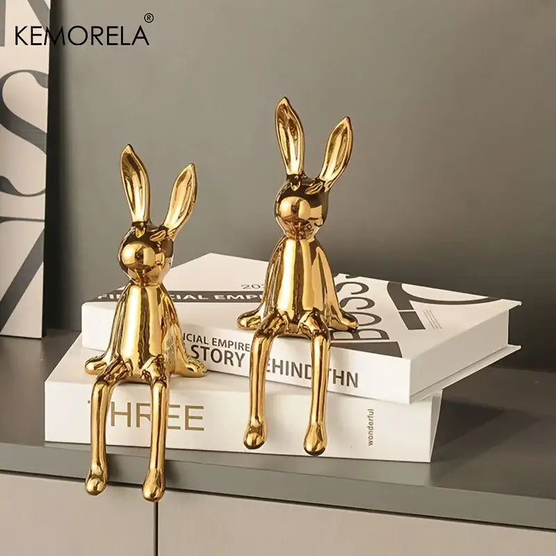 Two glossy gold ceramic sitting rabbit ornaments in varying sizes displayed on stacked books for living room decor
