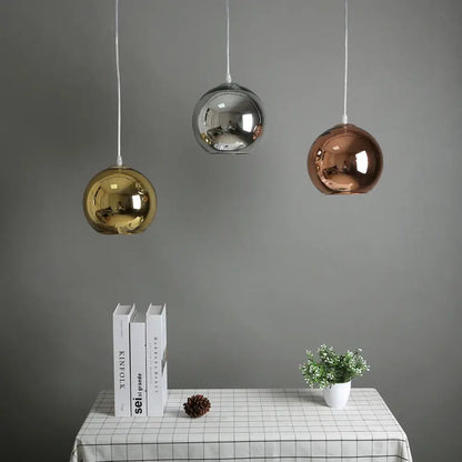 Modern golden ball glass pendant light trio with reflective gold silver and rose gold finishes hanging above table decorbites golden ball