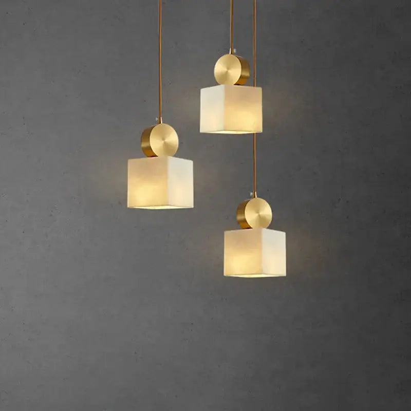 Three modern pendant lights with matte white square shades and polished brass accents for decorbites golden luxury marble pendant