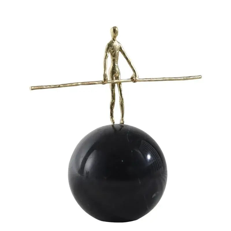 A slender golden metal abstract figure sculpture holding a rod on a black spherical base for living room decorbites decor