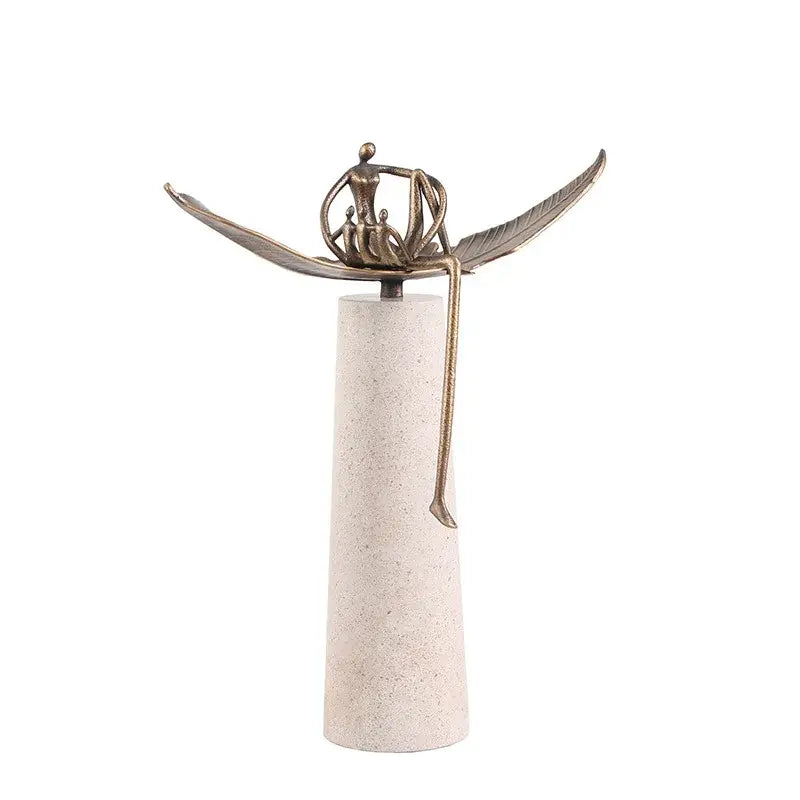 Bronze-colored decorbites golden metal abstract figure sculpture with outstretched wings on off-white pedestal for living room decor