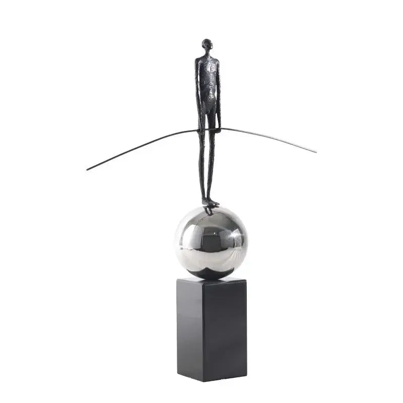 A sleek golden metal abstract figure sculpture balancing on a silver sphere for modern living room decor