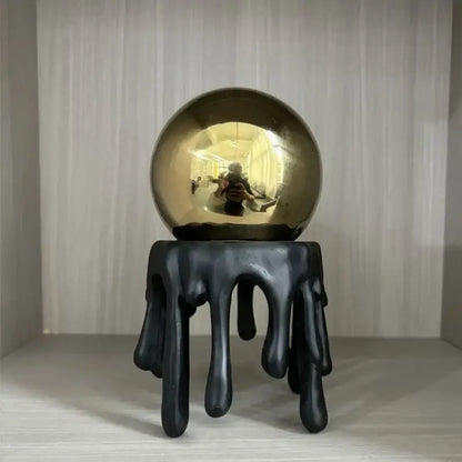 Shiny gold metallic sphere resting on a black dripping resin stand modern golden octopus spherical decorbites decor