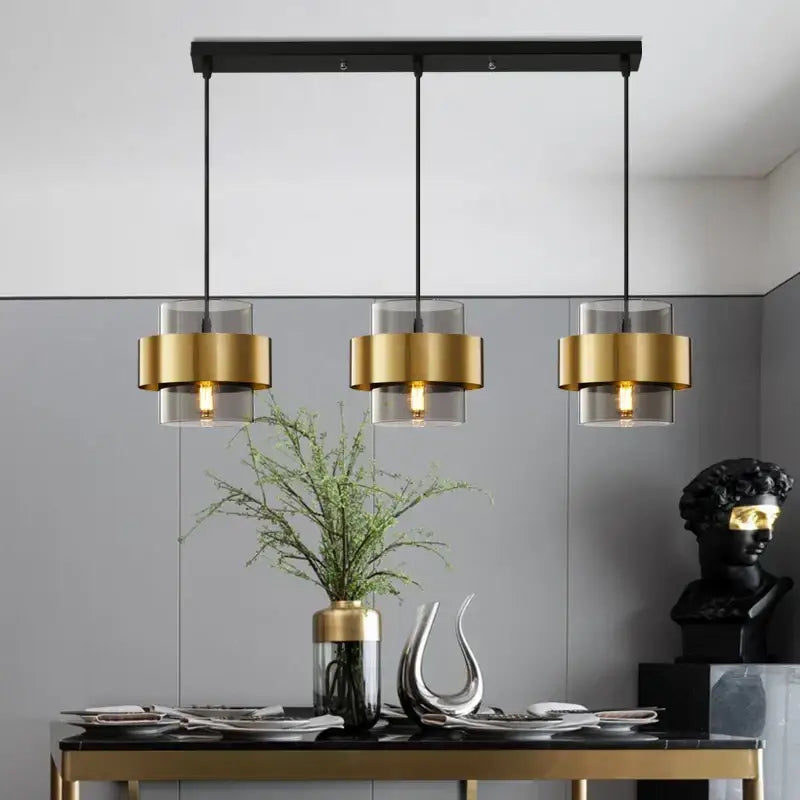Modern three-light pendant lights with black rectangular bar gold-toned cylindrical shades and clear glass diffusers by decorbites